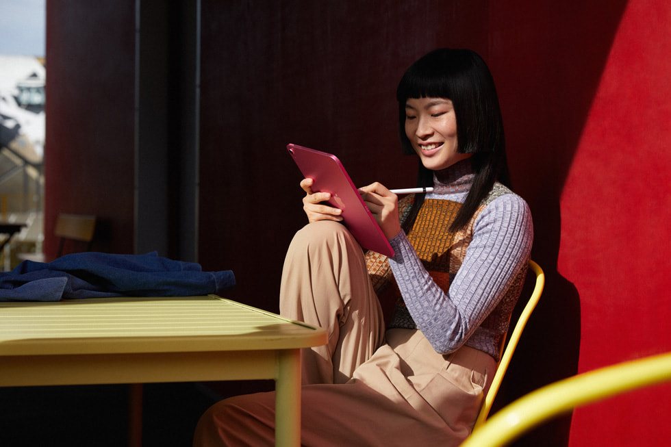 一位女士坐在办公桌上，使用 Apple Pencil 和一台粉色的 iPad。